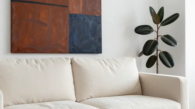 A partial view of a cream sofa with abstract wall art and a rubber plant in a bright living room