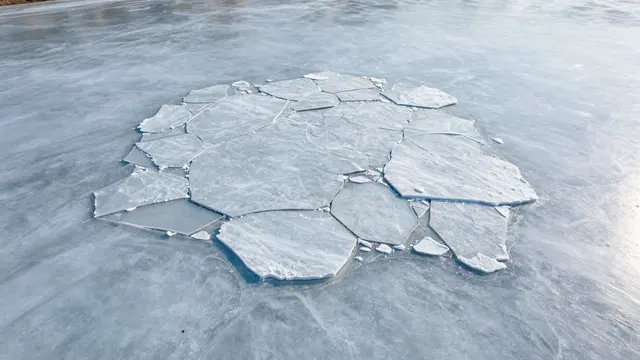 Aerial view of cracked flat ice floes resting on a frozen river surface in early spring