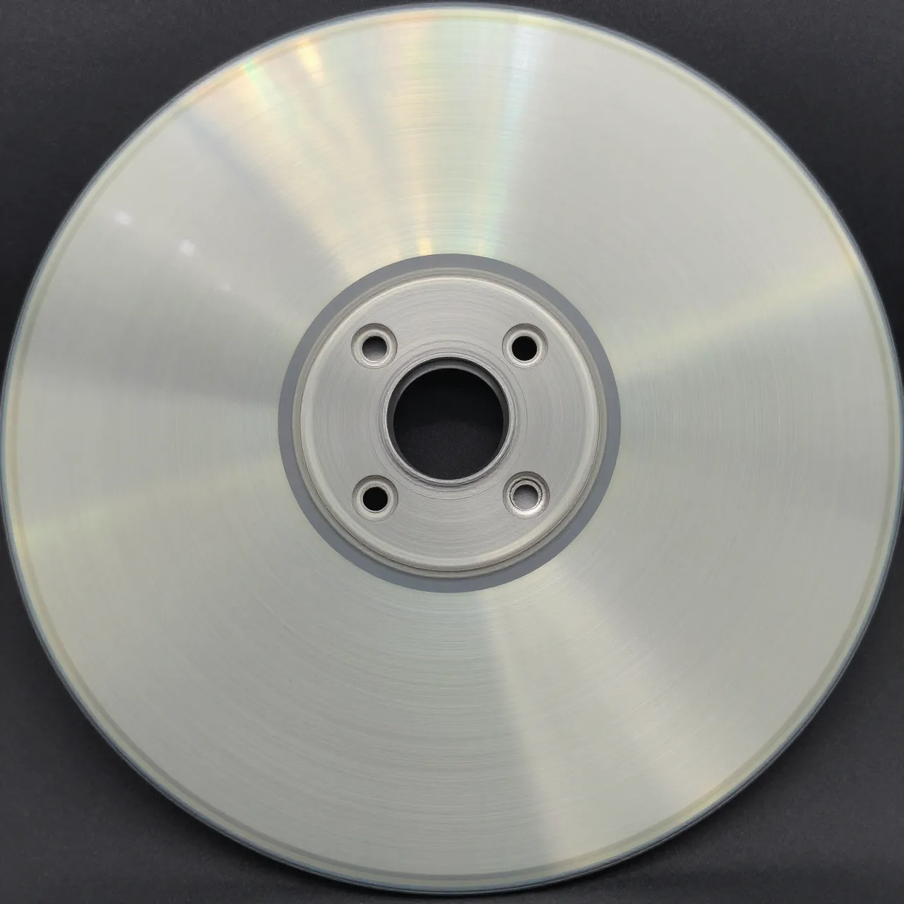 Close-up top view of a circular brushed aluminum disc with radial light reflections on a dark background