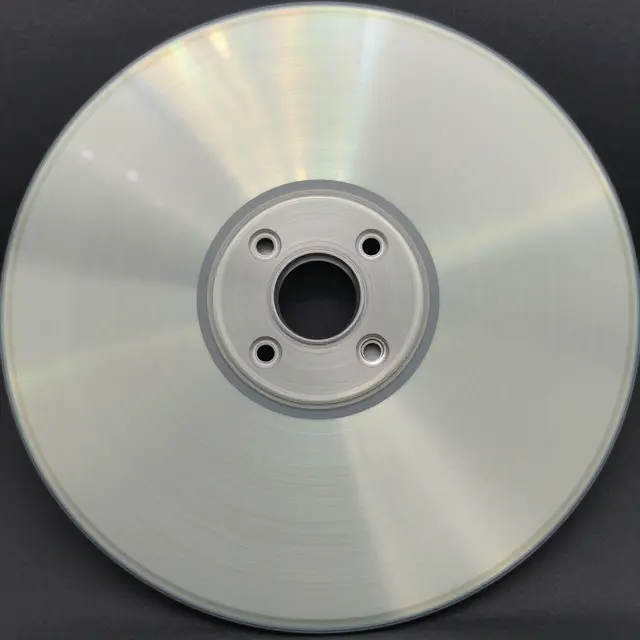 Close-up top view of a circular brushed aluminum disc with radial light reflections on a dark background
