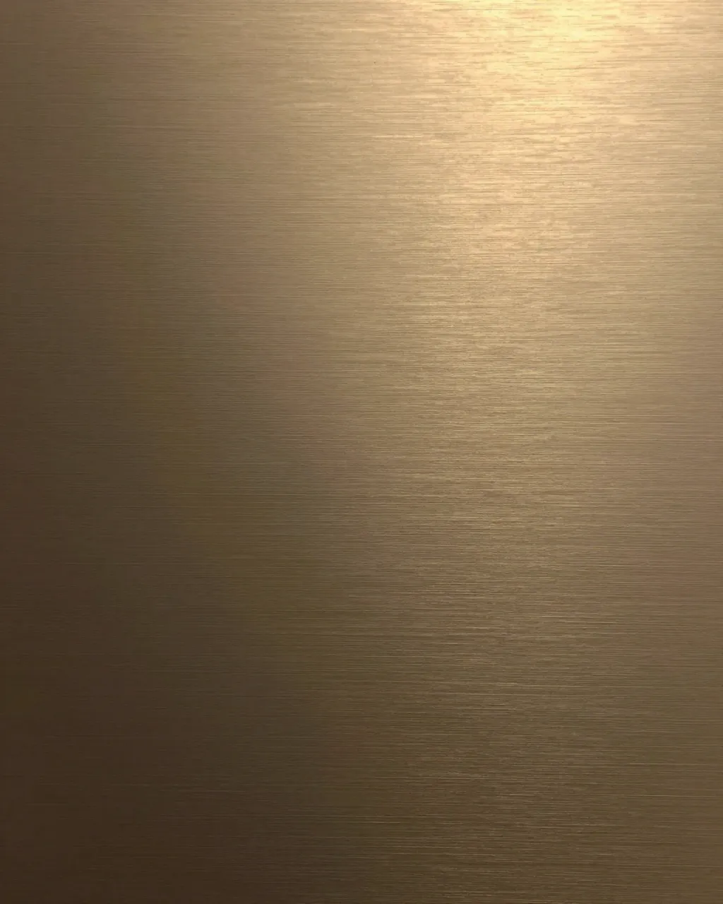 Close-up full frame view of brushed bronze metal with a soft warm upper right gradient reflection