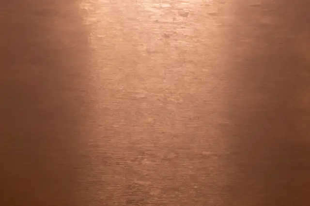 Warm brushed copper metal surface with subtle directional grain and soft center highlight