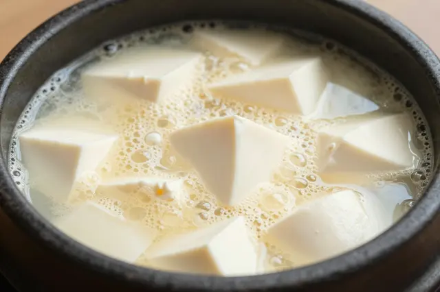 Close-up of bubbling soft tofu stew served in a dark black stone pot