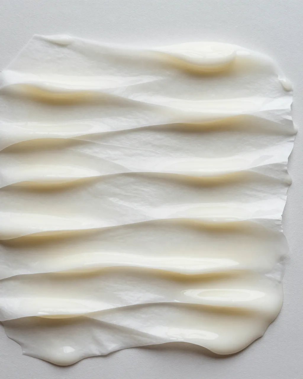 Full frame close-up of wet cream paper curled into soft even ripples against a pale neutral background