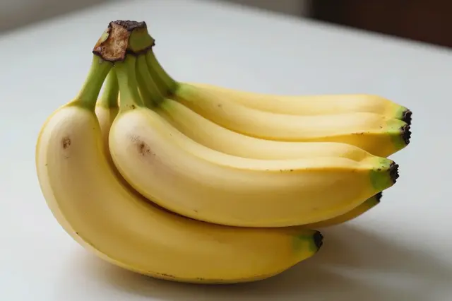A bunch of ripe yellow bananas rests on a smooth light table surface