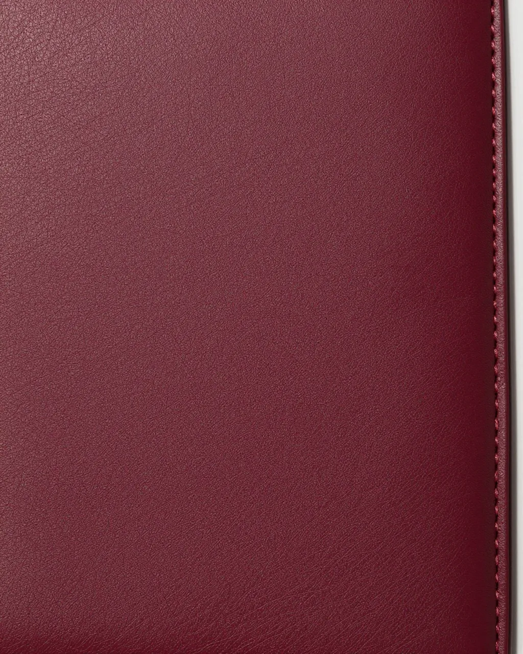 Close-up of fine-grained burgundy leather with a neat stitched seam running along its right edge