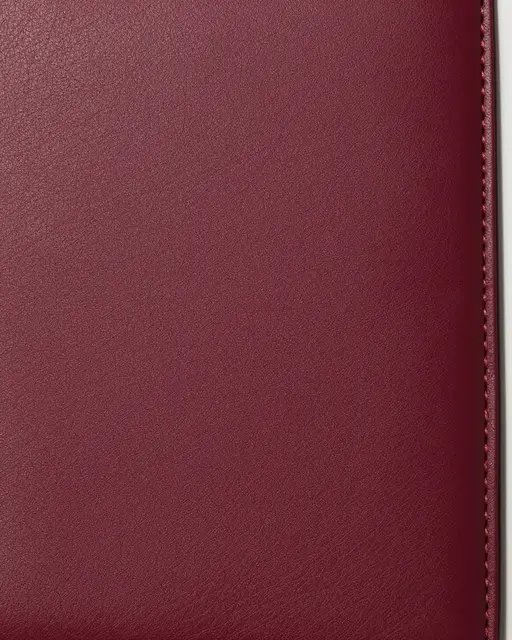 Close-up of fine-grained burgundy leather with a neat stitched seam running along its right edge