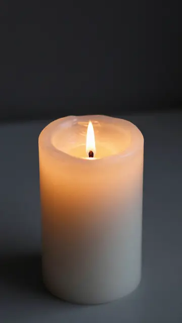 A lit white pillar candle glows softly against a muted dark gray background