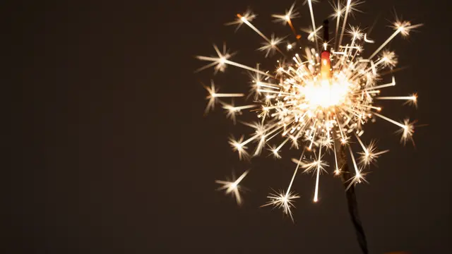 A lit sparkler emits golden light trails on the right, with empty dark copy space on the left
