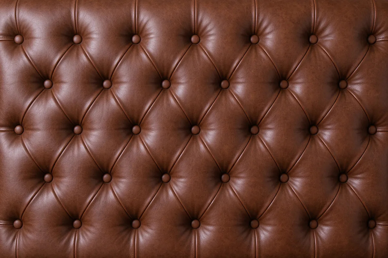 Full frame close-up of warm brown tufted leather upholstery with diamond pleats and round buttons