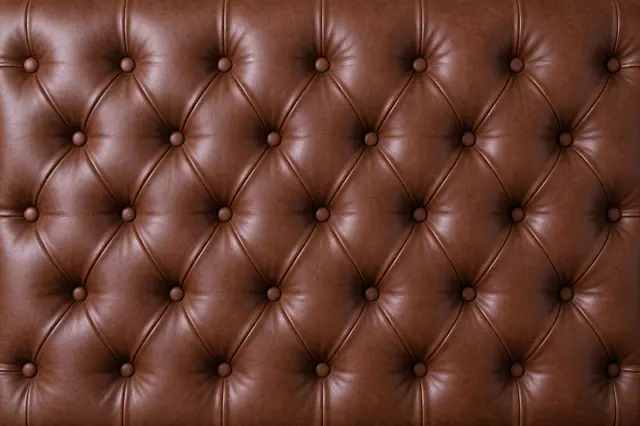 Full frame close-up of warm brown tufted leather upholstery with diamond pleats and round buttons