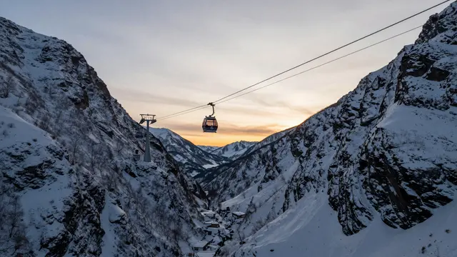A cable car gondola hangs on lines between snow covered mountain slopes at sunset.