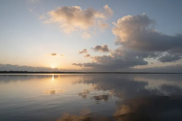 Glowing sunset clouds reflect perfectly on a still, mirror-smooth lake surface at dusk