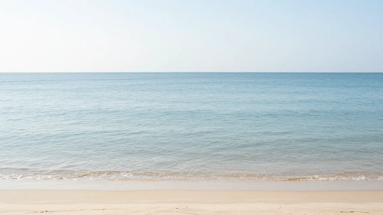 Gentle calm turquoise sea meets pale sandy shore under a soft pale sky