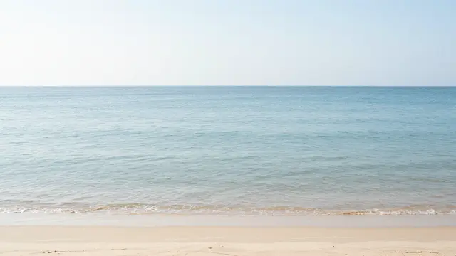 Gentle calm turquoise sea meets pale sandy shore under a soft pale sky
