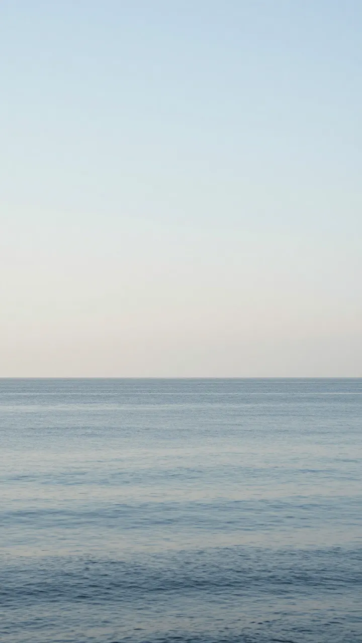 Minimal vertical view of a calm rippled sea under a vast soft gradient sky with low horizon.