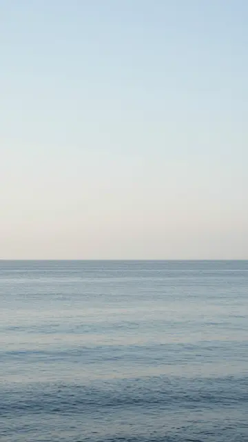 Minimal vertical view of a calm rippled sea under a vast soft gradient sky with low horizon.