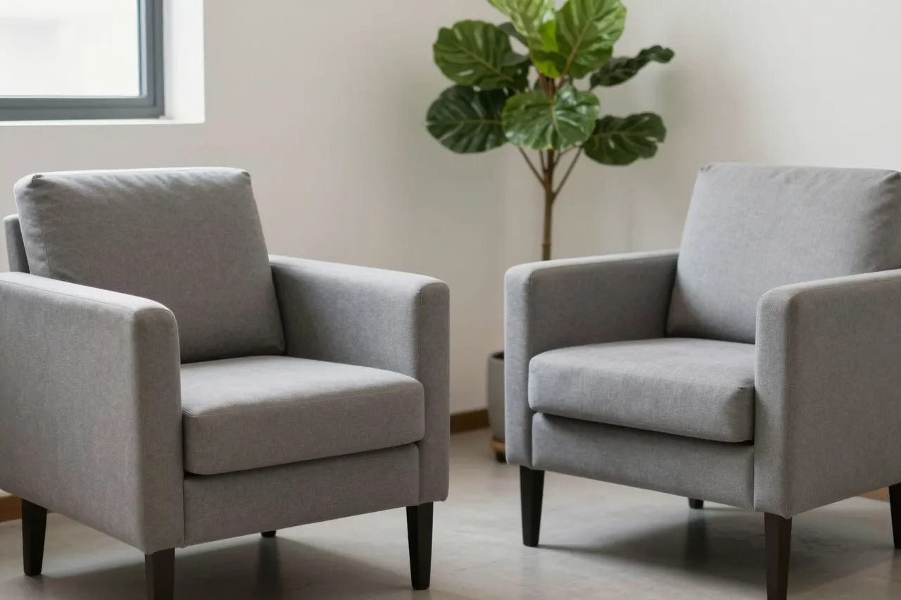Two gray upholstered armchairs sit beside a potted fiddle leaf fig plant in soft natural window light
