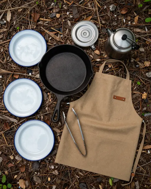 Flat lay of camp cooking equipment arranged on a pine needle forest floor