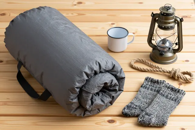 Flat lay arrangement of camping gear resting on a light wooden pine board surface