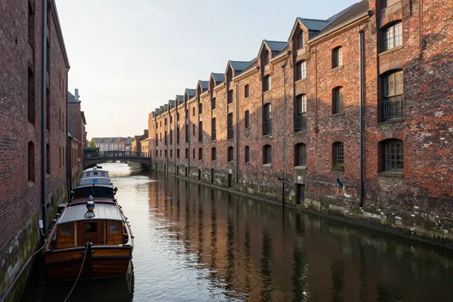 A quiet city canal lined with old brick warehouses and moored wooden boats in soft early morning light