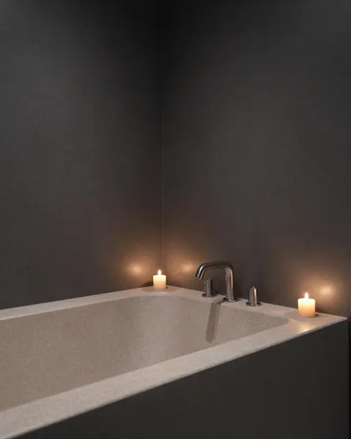 A light stone bathtub sits in a charcoal walled bathroom, lit by two small burning candles on its edge.