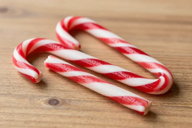 Red and white striped candy canes rest on a light brown wooden table surface