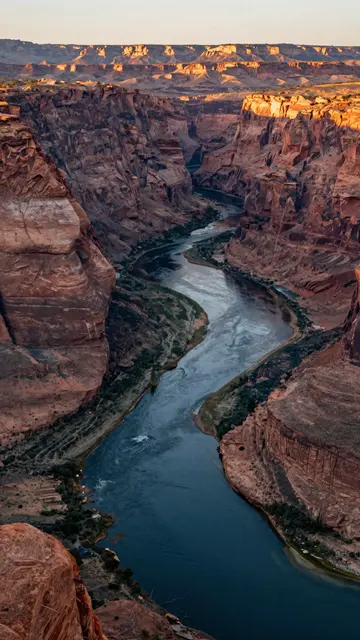A high-angle vertical view of a winding river cutting through red rock canyon walls at golden sunset