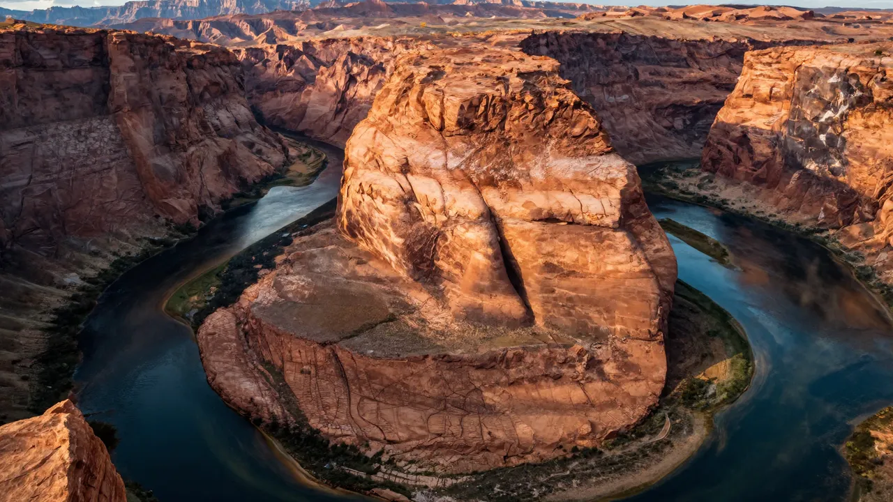 Aerial view of a horseshoe shaped canyon river bend lit by warm golden hour sunlight
