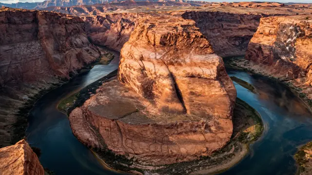 Aerial view of a horseshoe shaped canyon river bend lit by warm golden hour sunlight