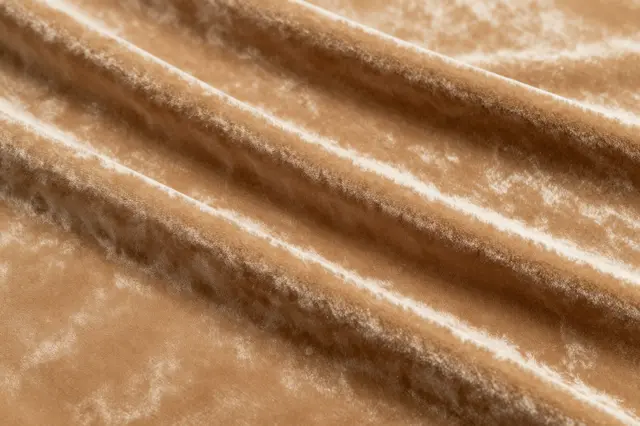 Close-up of draped caramel velvet fabric with soft diagonal folds and a subtle sheen