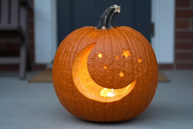 A glowing carved pumpkin with crescent moon and star cutouts sits on a home front porch.