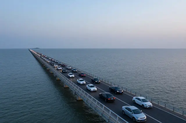Aerial view of cars traveling along a long sea causeway at soft dusk