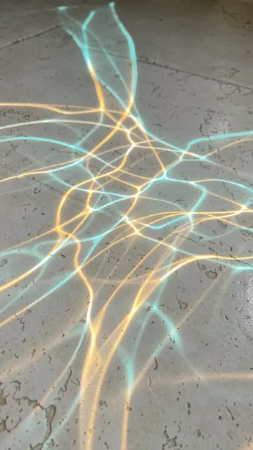 Wavering aqua and gold caustic light patterns stretch across a pale textured stone floor