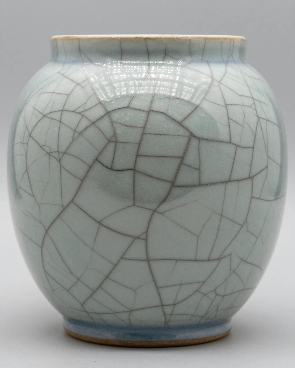 A small celadon ceramic vase with fine dark crackle glaze lines sits against a plain light gray background.