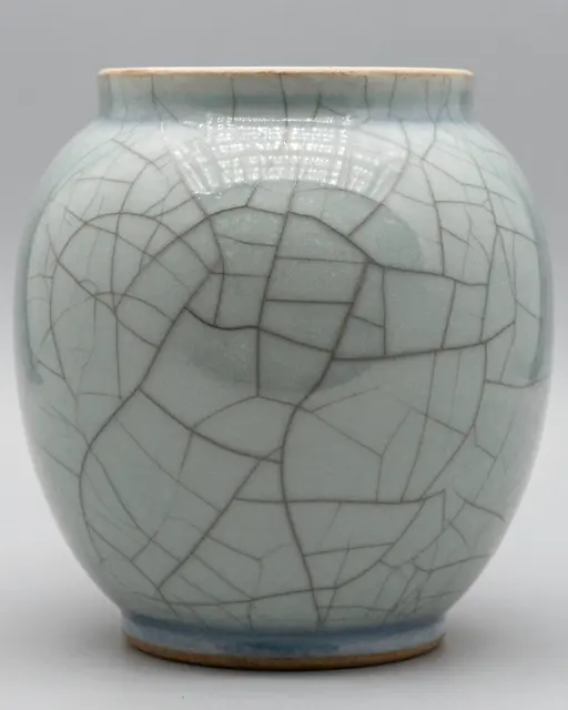 A small celadon ceramic vase with fine dark crackle glaze lines sits against a plain light gray background.
