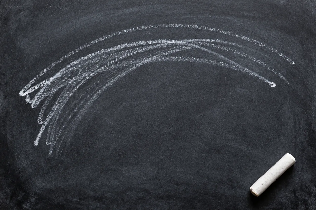 Curved white chalk smudge marks sit on a dark chalkboard with a loose stick of chalk in the corner