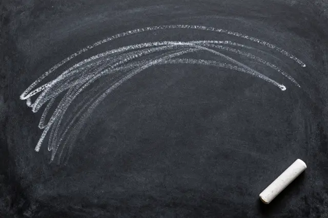 Curved white chalk smudge marks sit on a dark chalkboard with a loose stick of chalk in the corner