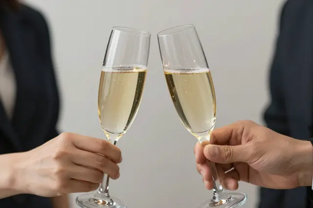 Two hands hold filled champagne flutes clinking together in a celebratory toast.