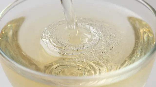 Liquid pours into a clear glass of pale champagne, creating swirling ripples and glistening bubbles