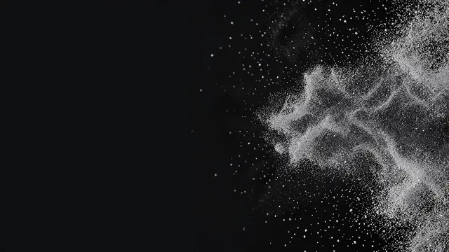 Fine silver dust drifts from the right edge of a dark charcoal background with empty copy space on the left