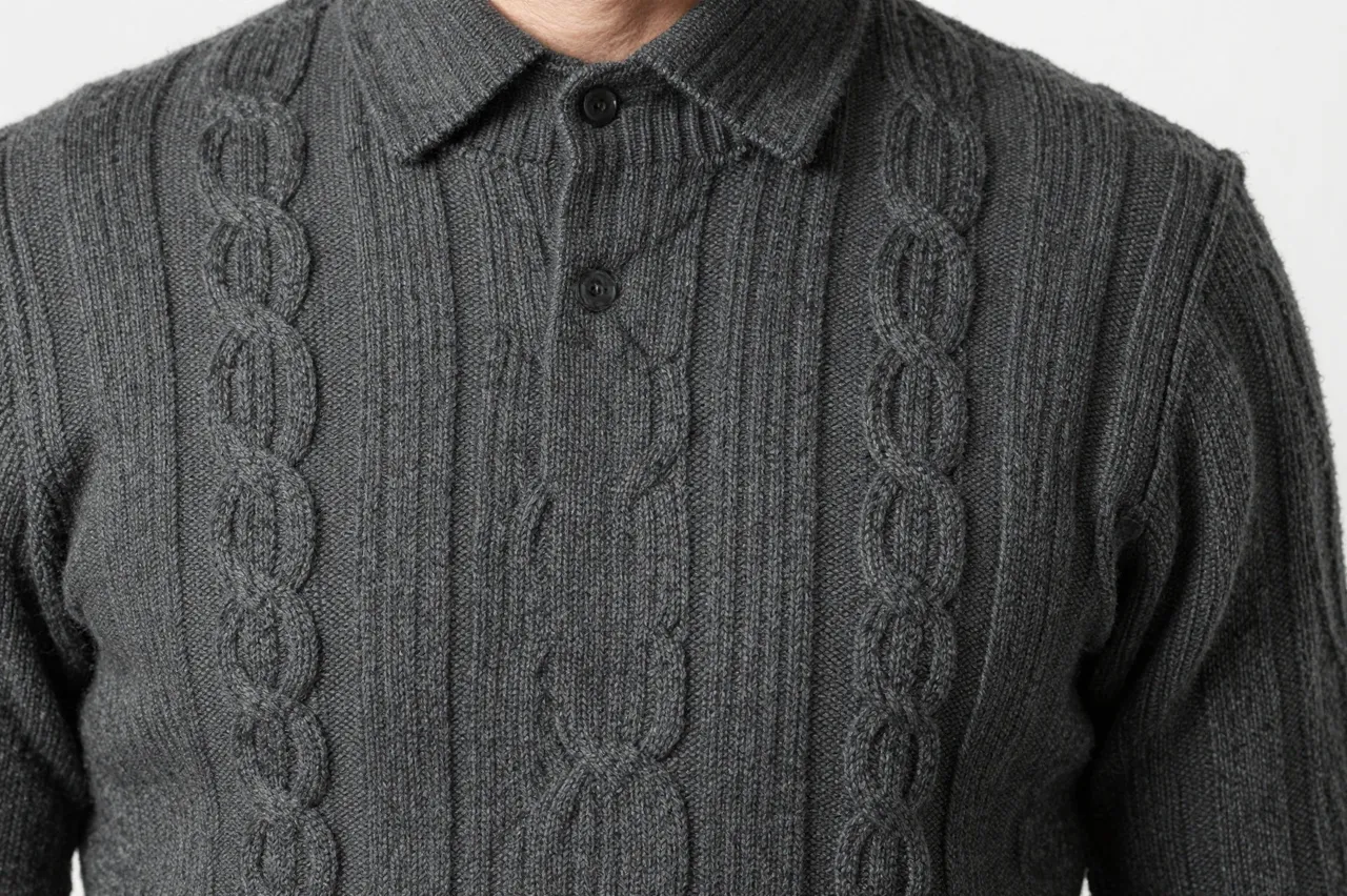 Close-up of a charcoal gray cable knit wool sweater with a polo collar against a plain light background