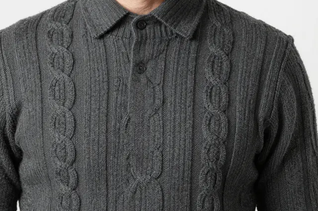 Close-up of a charcoal gray cable knit wool sweater with a polo collar against a plain light background