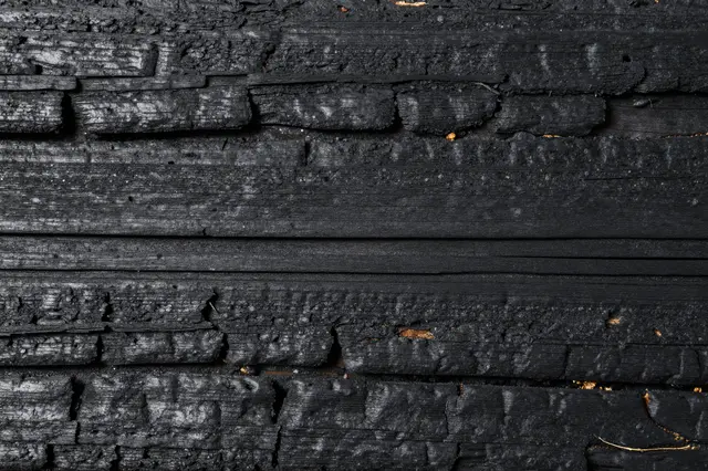 Close-up full frame of cracked, blackened charred wood planks with scattered exposed natural wood flecks