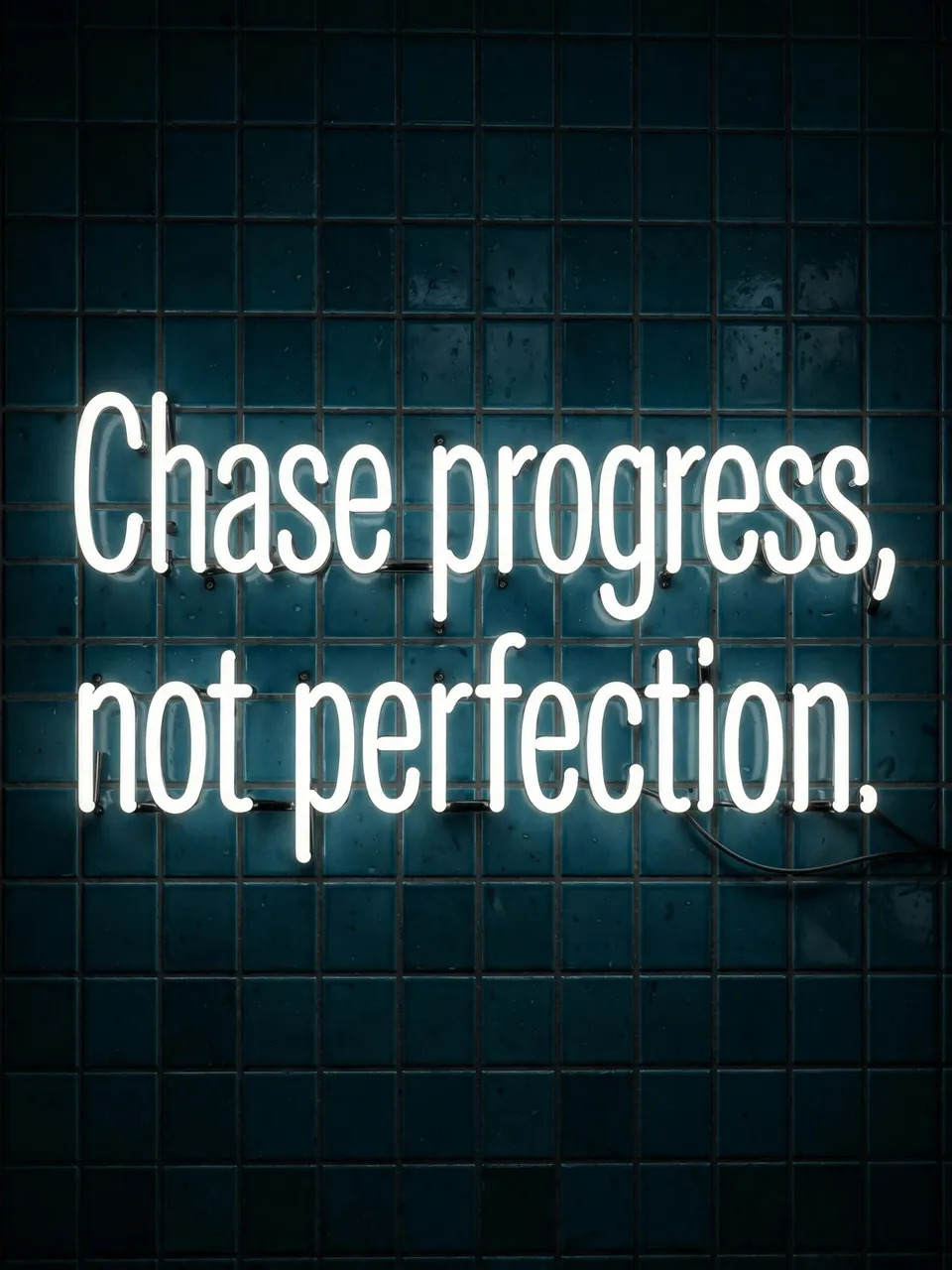 Glowing white neon sign reading "Chase progress, not perfection." mounted on a dark teal tiled wall