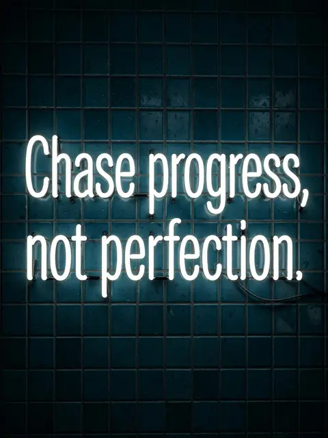 Glowing white neon sign reading "Chase progress, not perfection." mounted on a dark teal tiled wall