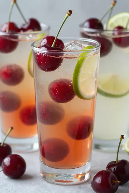 Tall glasses of sparkling cherry limeade garnished with fresh cherries and lime slices on a light countertop