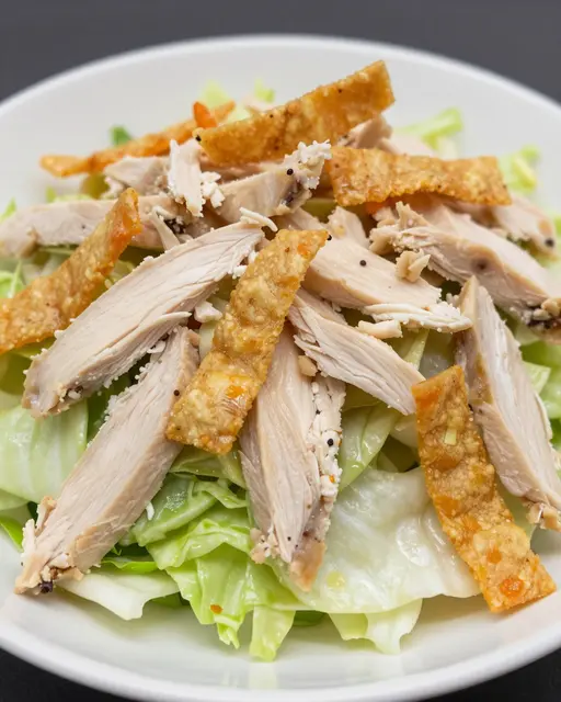 Close-up view of a chicken salad topped with crispy wonton strips served in a white bowl