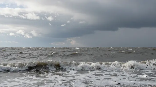 Turbulent gray sea with breaking waves sits beneath a heavy, dramatic overcast winter sky.