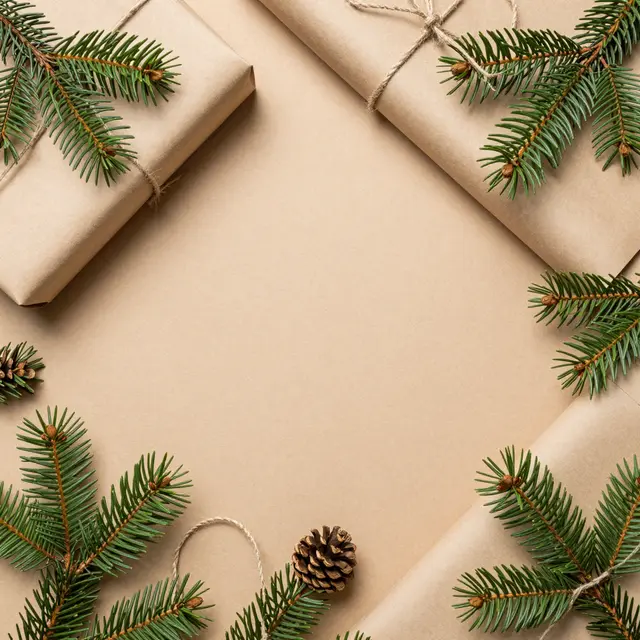 Top view framed Christmas flat lay with kraft wrapped gifts, pine sprigs, twine, and empty central copy space on a tan